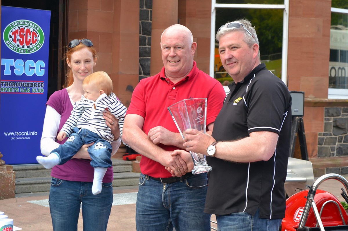 Gerard O'Connell {R} receives the winners trophy from Simon McKinley's father Peter, his widow Diedre and baby son Rory